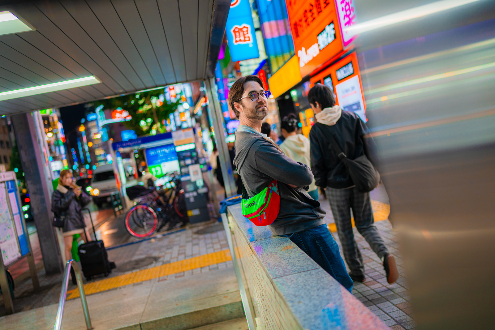 Aydrian leaning against a ledge on a neon-lit Tokyo street at night — leaning into technical consulting.